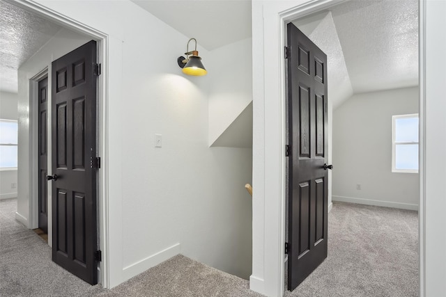 hall with vaulted ceiling, a textured ceiling, and light colored carpet