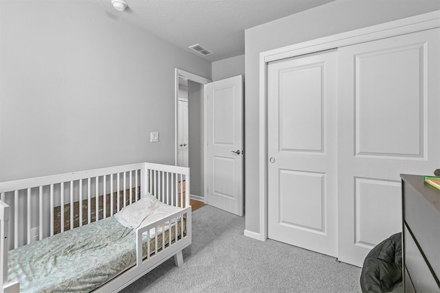 carpeted bedroom with a textured ceiling, a closet, and a nursery area