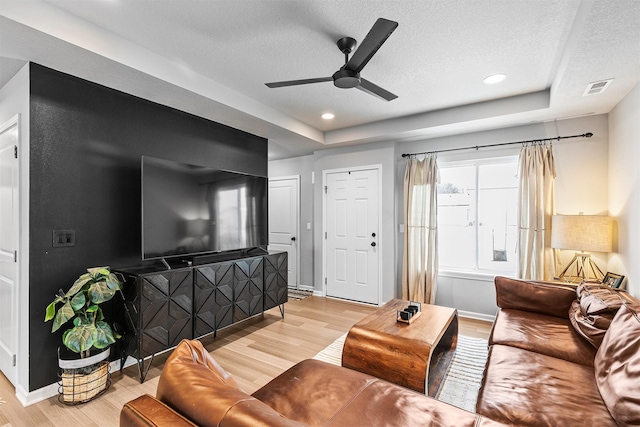 living room featuring ceiling fan, light hardwood / wood-style flooring, a tray ceiling, and a textured ceiling