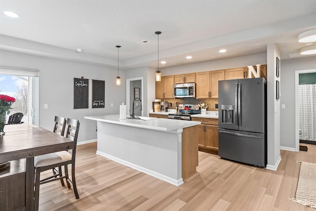 kitchen featuring a center island with sink, hanging light fixtures, light wood-type flooring, stainless steel appliances, and sink