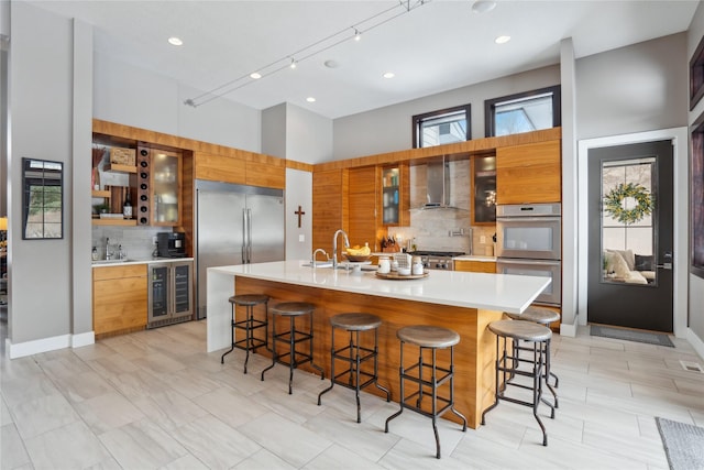 kitchen featuring appliances with stainless steel finishes, wall chimney range hood, a spacious island, a kitchen bar, and wine cooler