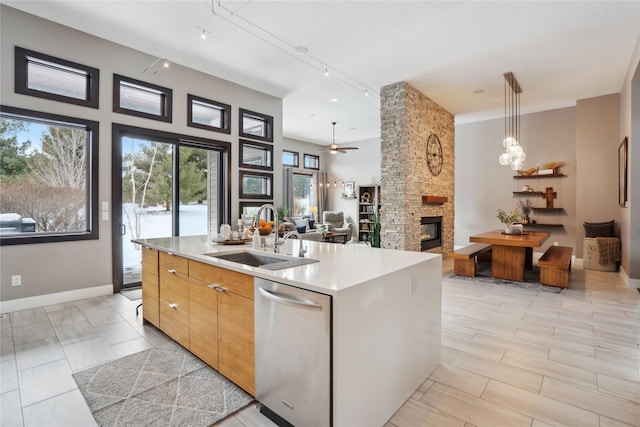 kitchen featuring a center island with sink, decorative light fixtures, a stone fireplace, sink, and dishwasher