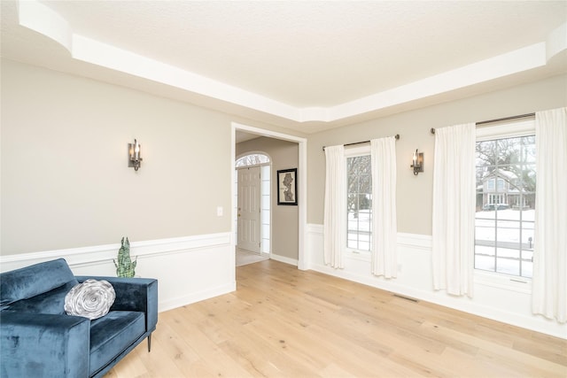 living area featuring a raised ceiling, light wood-type flooring, and plenty of natural light