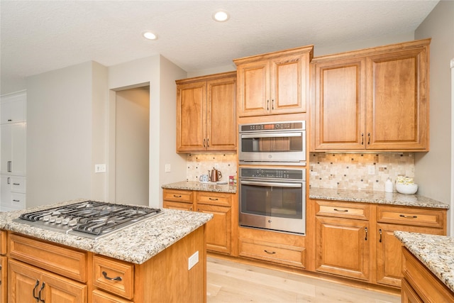 kitchen with stainless steel appliances, light stone countertops, light hardwood / wood-style floors, a textured ceiling, and decorative backsplash