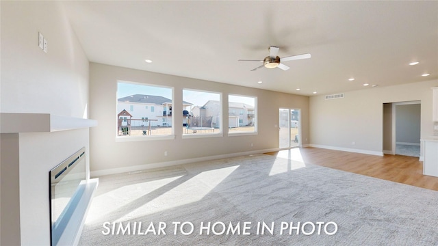 unfurnished living room featuring a wealth of natural light, ceiling fan, and light colored carpet