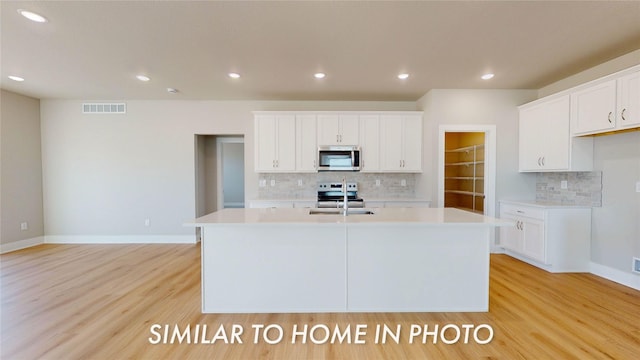 kitchen featuring white cabinets, an island with sink, appliances with stainless steel finishes, and light hardwood / wood-style floors