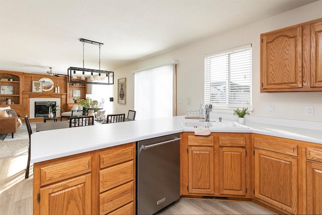 kitchen with light wood-type flooring, kitchen peninsula, decorative light fixtures, sink, and stainless steel dishwasher