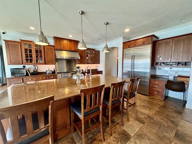 kitchen with hanging light fixtures, stove, built in refrigerator, sink, and a large island with sink