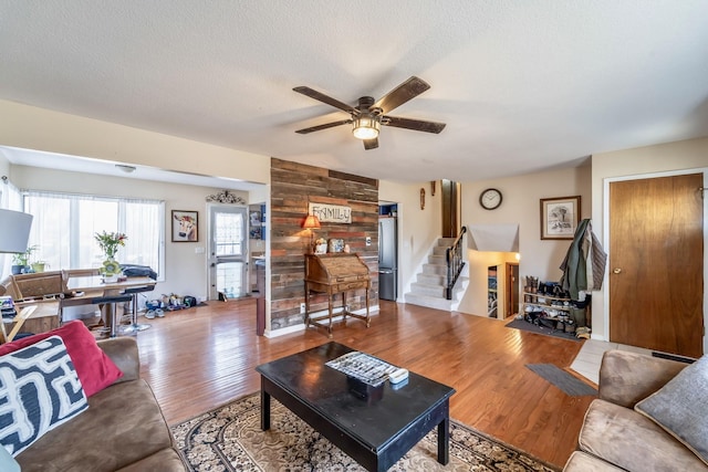 living room featuring a textured ceiling, wooden walls, ceiling fan, and light hardwood / wood-style flooring