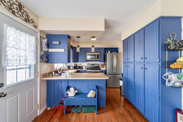 kitchen with appliances with stainless steel finishes, blue cabinetry, dark hardwood / wood-style flooring, kitchen peninsula, and hanging light fixtures