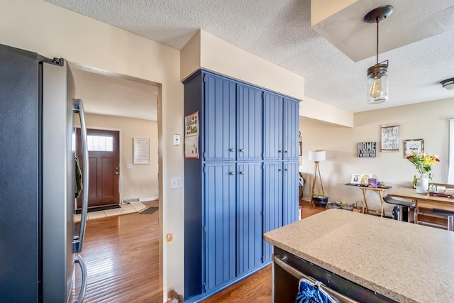 kitchen featuring stainless steel refrigerator, blue cabinets, a textured ceiling, and hardwood / wood-style floors