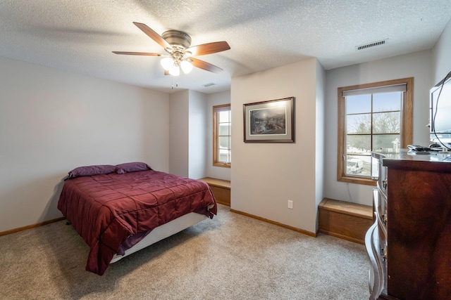 bedroom with ceiling fan, multiple windows, a textured ceiling, and light colored carpet