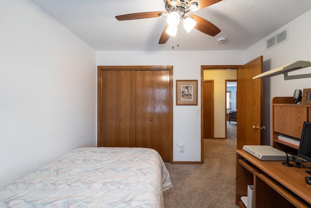 bedroom with ceiling fan, a closet, a textured ceiling, and light colored carpet