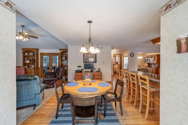 dining area with ceiling fan with notable chandelier, light hardwood / wood-style flooring, french doors, and a textured ceiling