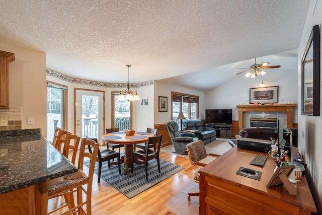 dining space with light hardwood / wood-style flooring, vaulted ceiling, a textured ceiling, a tile fireplace, and ceiling fan with notable chandelier