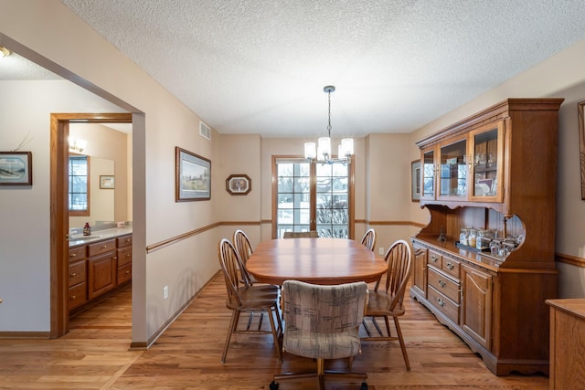 dining space with a notable chandelier, light hardwood / wood-style flooring, a textured ceiling, and a wealth of natural light