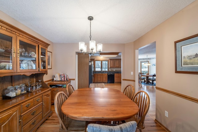 dining area featuring sink, a textured ceiling, an inviting chandelier, and light hardwood / wood-style floors