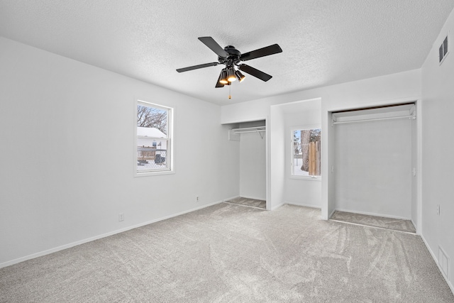 unfurnished bedroom with light carpet, ceiling fan, multiple closets, and a textured ceiling