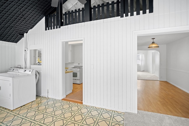 clothes washing area with hardwood / wood-style flooring, washing machine and dryer, and a high ceiling