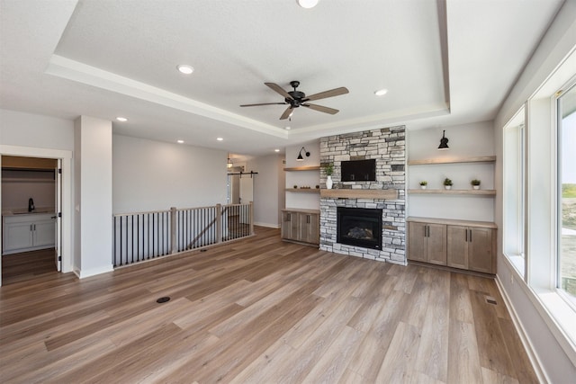 18274 Hidden Knl, Clive, IA 50325 - unfurnished living room featuring a raised ceiling, a ceiling fan, light wood-type flooring, a barn door, and recessed lighting