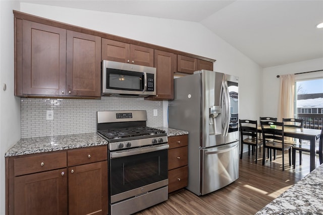 kitchen with light stone counters, dark wood-style flooring, decorative backsplash, appliances with stainless steel finishes, and vaulted ceiling