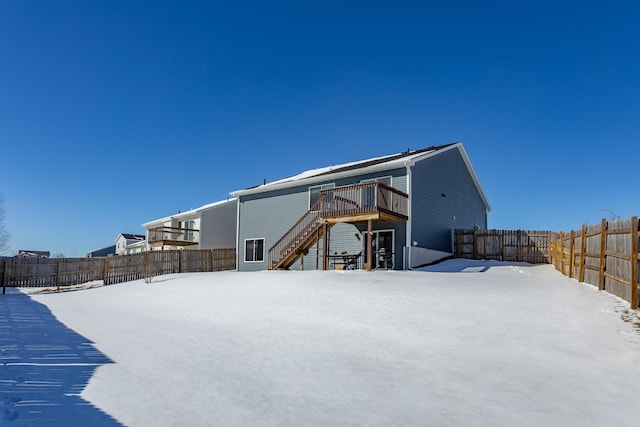 snow covered back of property featuring a deck, fence, and stairway