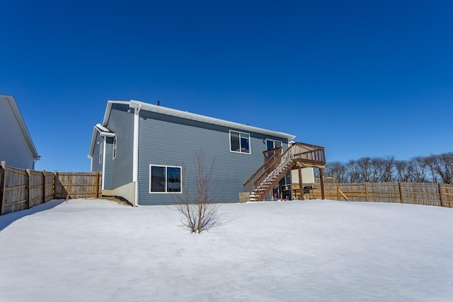 snow covered back of property featuring stairs, a deck, and a fenced backyard