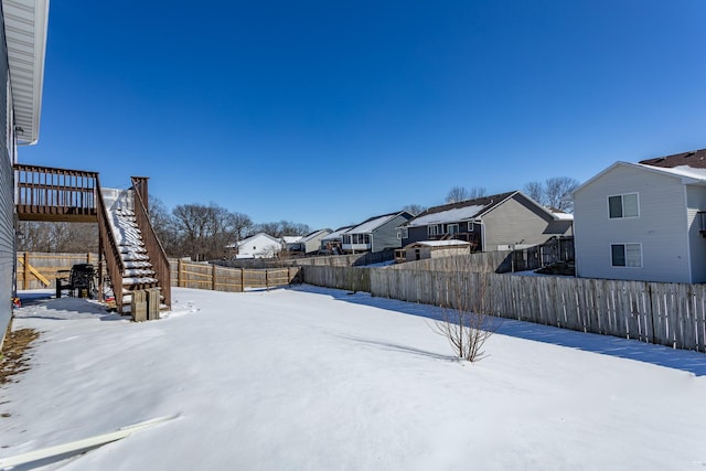 yard covered in snow with a residential view, a fenced backyard, and stairs