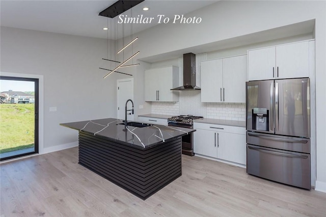 kitchen featuring white cabinets, a kitchen island with sink, stainless steel appliances, wall chimney range hood, and backsplash