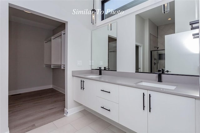 bathroom with a sink, baseboards, double vanity, and a shower stall