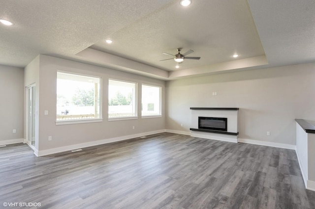 1020 2nd St NE, Altoona, IA 50009 - unfurnished living room featuring a tray ceiling, a textured ceiling, a ceiling fan, wood finished floors, and a glass covered fireplace