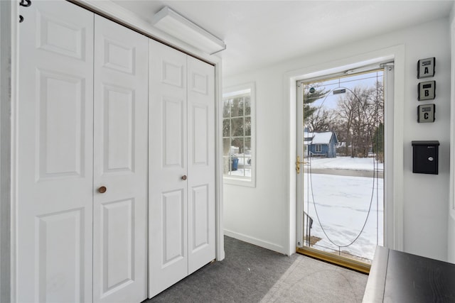 doorway to outside featuring baseboards and dark colored carpet