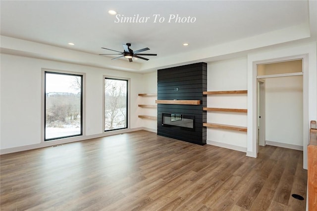 unfurnished living room with a raised ceiling, a fireplace, baseboards, and wood finished floors