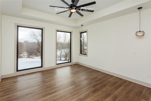 spare room featuring dark wood-type flooring, a raised ceiling, visible vents, and baseboards