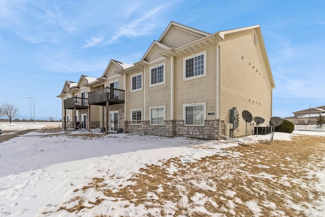 snow covered rear of property featuring stone siding and a balcony