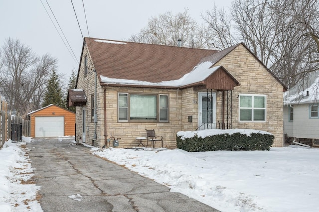 view of front of house with roof with shingles, a detached garage, stone siding, an outdoor structure, and driveway