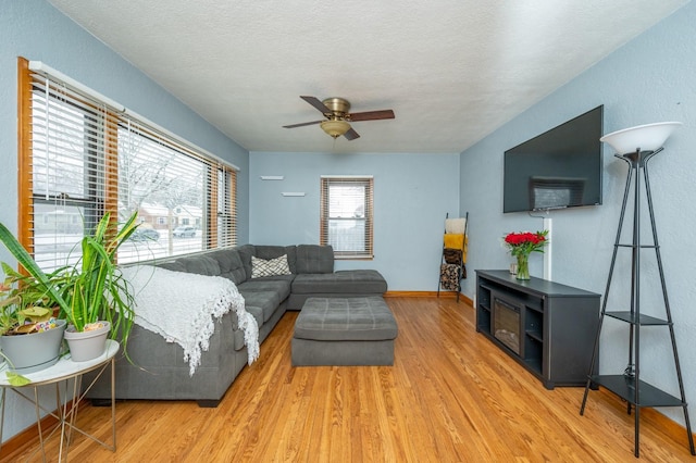 living room with a ceiling fan, a textured ceiling, baseboards, and wood finished floors