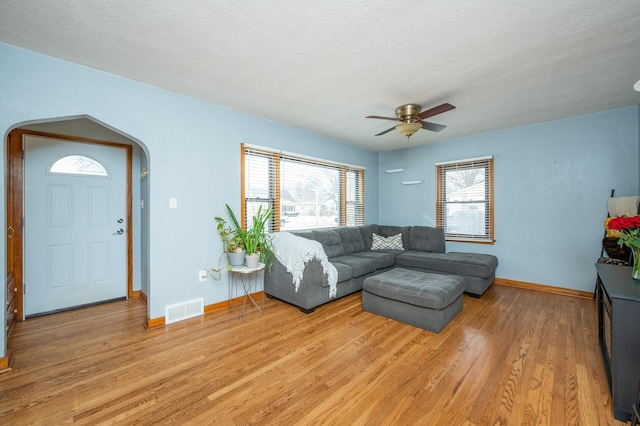 living room with arched walkways, light wood-type flooring, visible vents, and baseboards