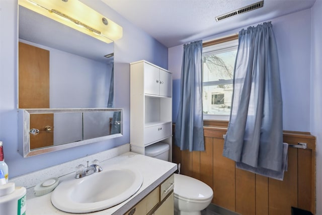 half bath with toilet, vanity, and visible vents