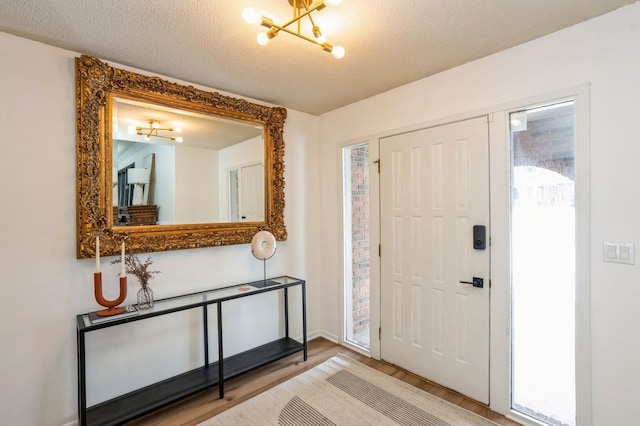 entrance foyer featuring a textured ceiling, baseboards, wood finished floors, and a notable chandelier