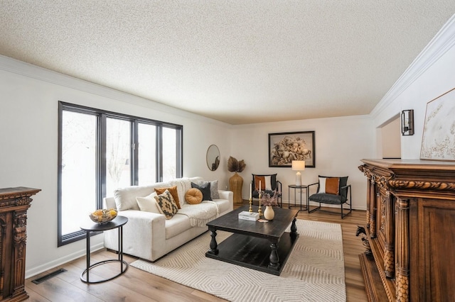 living area featuring a textured ceiling, visible vents, baseboards, light wood-style floors, and ornamental molding