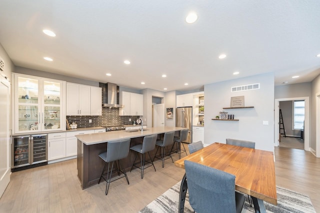 kitchen with white cabinets, wall chimney exhaust hood, high quality fridge, light countertops, and a sink