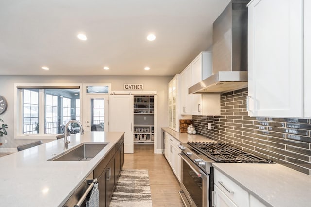 kitchen featuring backsplash, white cabinets, a sink, high end stove, and wall chimney exhaust hood