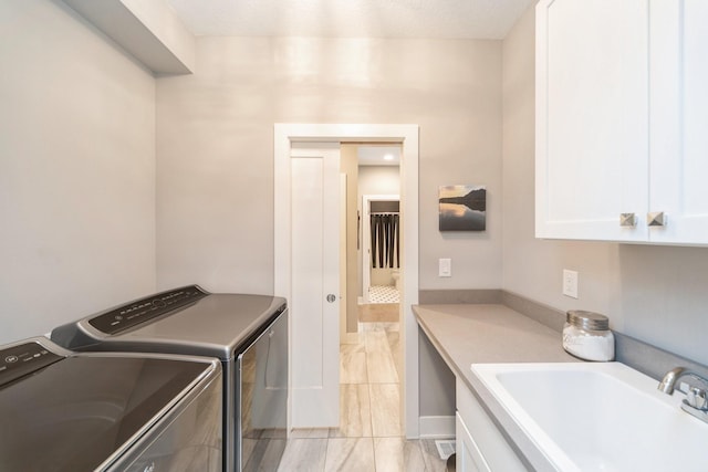 clothes washing area featuring a textured ceiling, washer and clothes dryer, a sink, and cabinet space