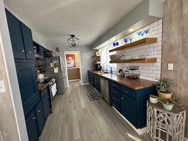 kitchen with butcher block counters, appliances with stainless steel finishes, blue cabinetry, open shelves, and a sink