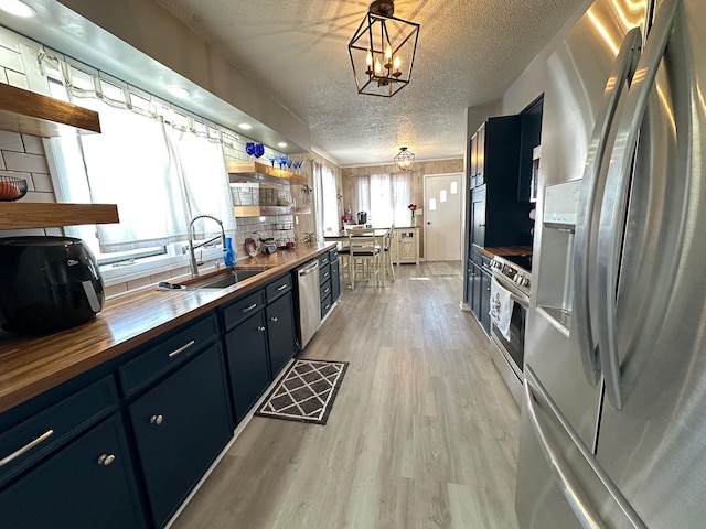 kitchen with stainless steel appliances, butcher block counters, a sink, hanging light fixtures, and open shelves