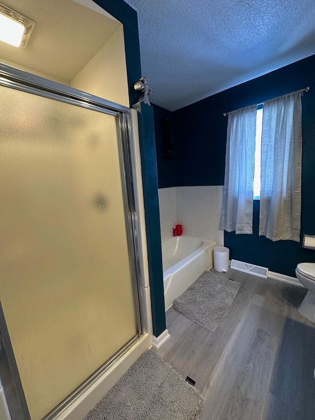 full bath with a textured ceiling, wood finished floors, visible vents, a bath, and a stall shower