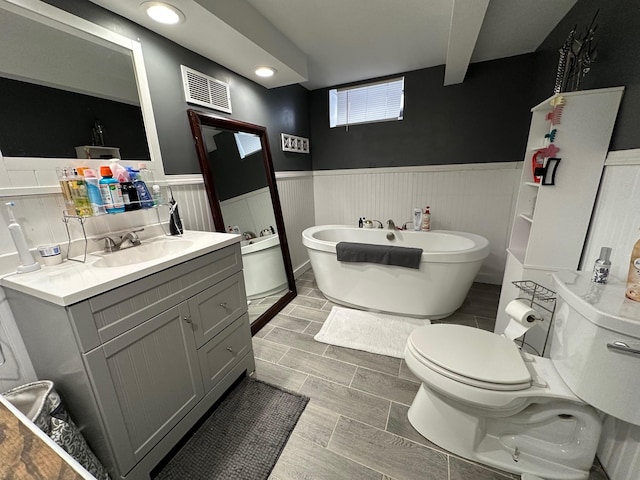 bathroom with a wainscoted wall, a freestanding bath, visible vents, and vanity