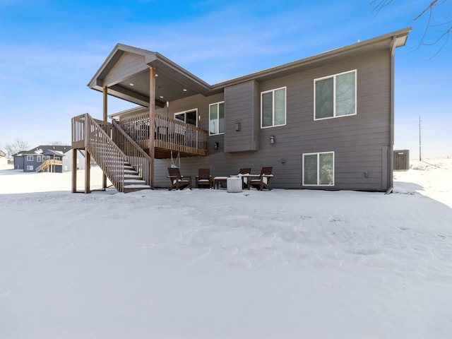 snow covered house with a deck, stairway, and cooling unit