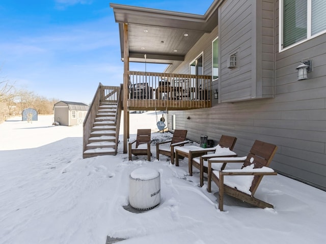 snow covered patio featuring an outbuilding, a shed, and stairway